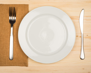 plate, knife and fork at napkin on wooden background
