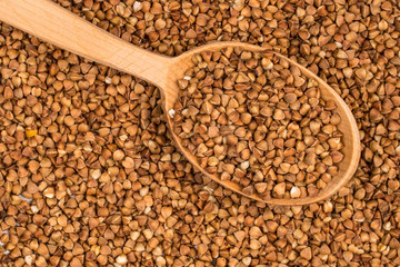 Buckwheat in a wooden spoon on buckwheat background.