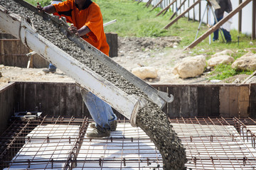 Trabajador vertiendo concreto desde una mezcladora para fundir la placa de los cimientos de una...