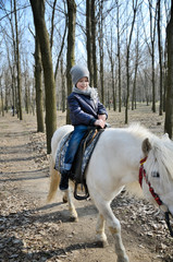 smiling boy riding a white pony trail in the park in spring