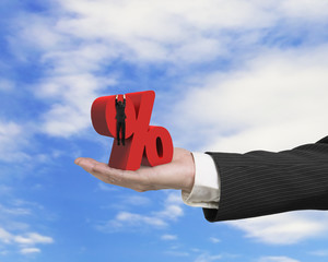 Hand showing businessman hanging on percentage sign with sky clo