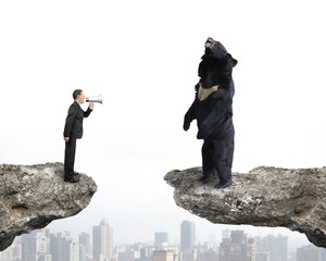 Businessman yelling at black bear on cliff with cityscape