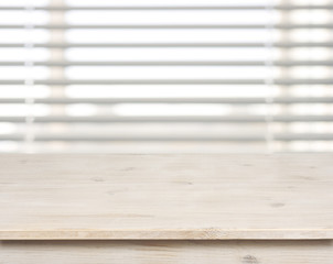 Wooden table on defocuced window with venetian blinds background