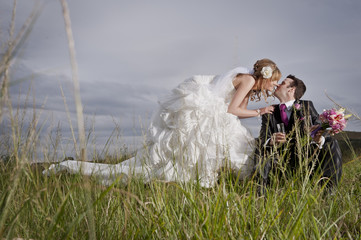 Happy newly wed couple outdoors in field of long grass kissing