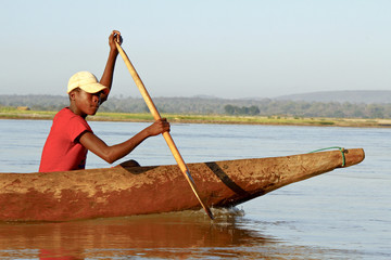 Fototapeta na wymiar Young Malagasy african boy rowing traditional canoe on river