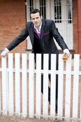 Handsome young groom outdoors with drink against white fence