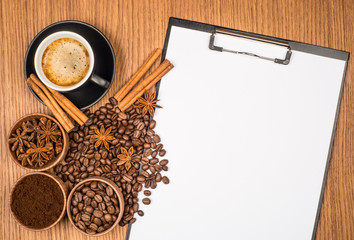 A cup of coffee, star anise, cinnamon and a clipboard with blank