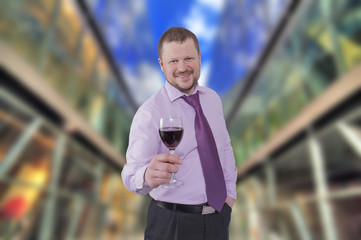 Businessman holding glass of wine with modern shopping mall in