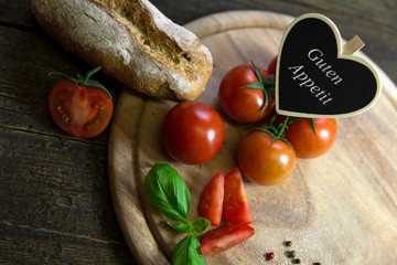 Tomaten mit Brotlaib auf Holztisch, Herz mit Text Guten Appetit - obrazy, fototapety, plakaty