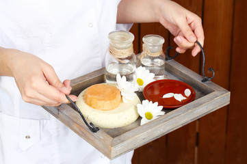 Beauty therapist holding tray of spa treatments, close-up, on wooden wall background