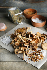 Dried mushrooms with spices on paper on wooden table, closeup