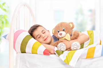 Obraz na płótnie Canvas Lovely boy sleeping with a teddy bear in a bed