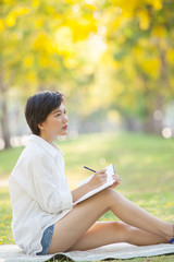 young woman sitting on green grass park with pencil and note boo