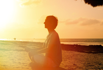 young man meditating at sunset beach