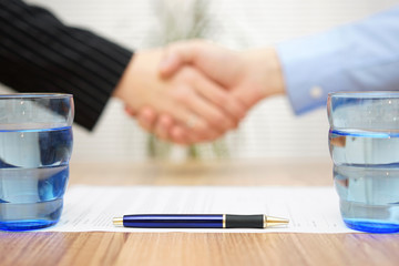 signed contract with handshake in blur, focus on pen