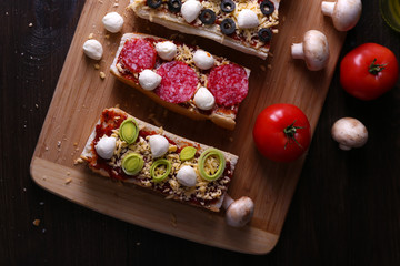 Different sandwiches with vegetables and cheese on cutting board on table close up