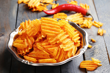 Delicious potato chips on plate on wooden table close-up