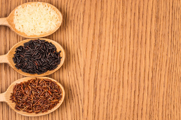 Red, white, and black rice in a wooden spoon on a wooden table