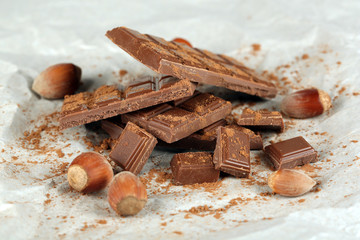 Pieces of chocolate with cocoa on parchment, closeup