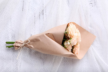 Bouquet of fresh roses wrapped in paper on wooden background