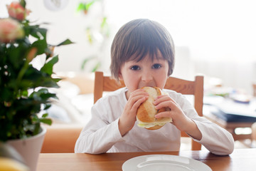 Beautiful little boy, eating sandwich at home, vegetables on the