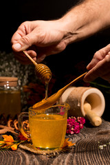 Honey dripping from a wooden honey dipper in a jar from man hand