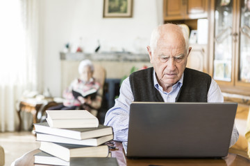 Senior man looking for information in books and internet - 81176010