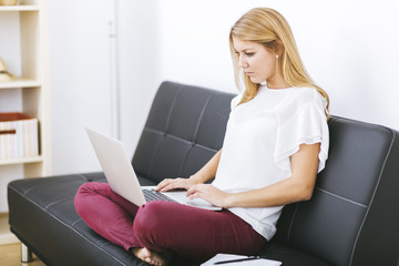 young woman looking on your laptop sitting on sofa at home
