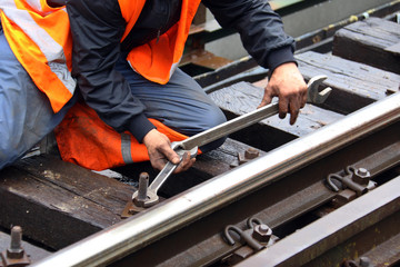 Worker tightens the screw on railroad with two spanners in hands - obrazy, fototapety, plakaty
