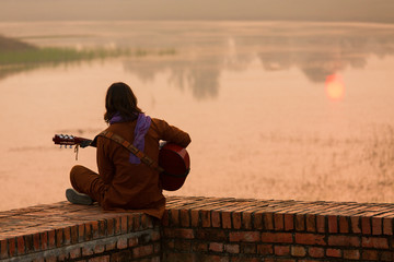 Young man singer singing on his guitar on the lake at a beautifu