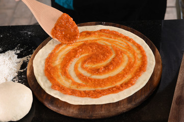 close up of adding tomato sauce to pizza base