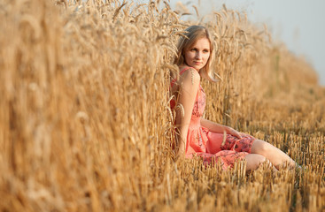 Young beautiful girl sitting on the hay in field