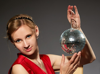 Young woman holding disco ball sitting on grey background