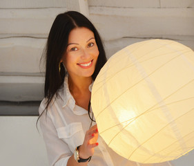 Young smiling woman standing near lamp , in the house