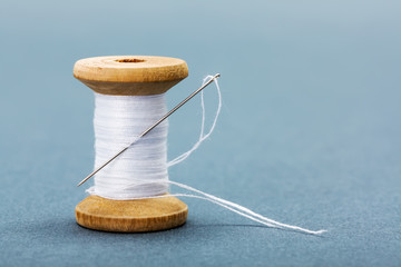 Spool of white sewing thread and needle