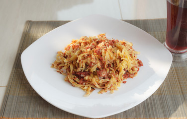 Pasta with fried meat on white plate and glass of juice