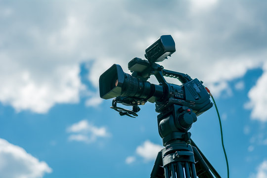 Professional video camera on a tripod against the blue sky