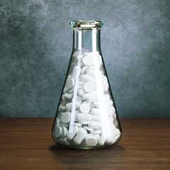 Erlenmeyer flask full of pills or tablets behind old grey wall