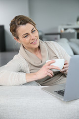 Mature woman relaxing with cup of coffee in front of laptop