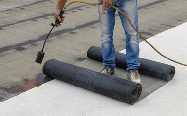 Worker preparing part of bitumen roofing felt roll