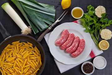 raw fresh sausage with cooking ingredients and pasta in pan