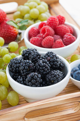 fresh berries and green grapes on a wooden tray, vertical