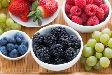 fresh berries in a bowl and green grapes on wooden tray, closeup