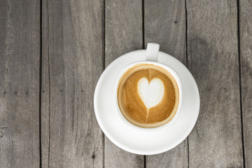 A cup of coffee with heart pattern in a white cup on wooden back