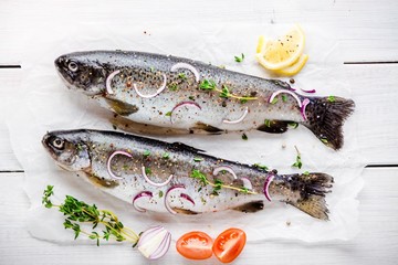two raw trouts on paper with thyme and red onion slices