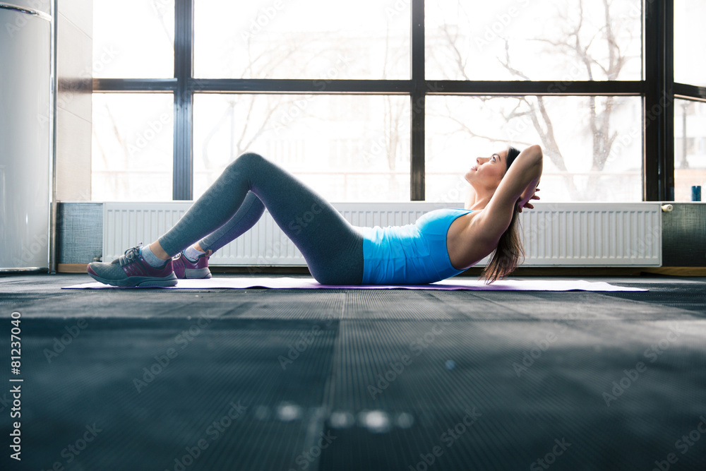 Wall mural Young woman lying on the yoga mat and doing fitness exercise