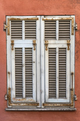 Closed white weathered window shutters on a red wall