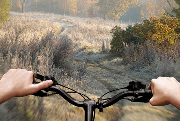 A cyclist's hands on the handlebars against a dirt road landscape. View from the cyclist's side.