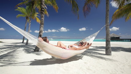 couple relaxing in hammock on tropical beach - Powered by Adobe