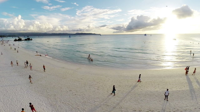 Aerial flight over sandy beach, waves and tourists